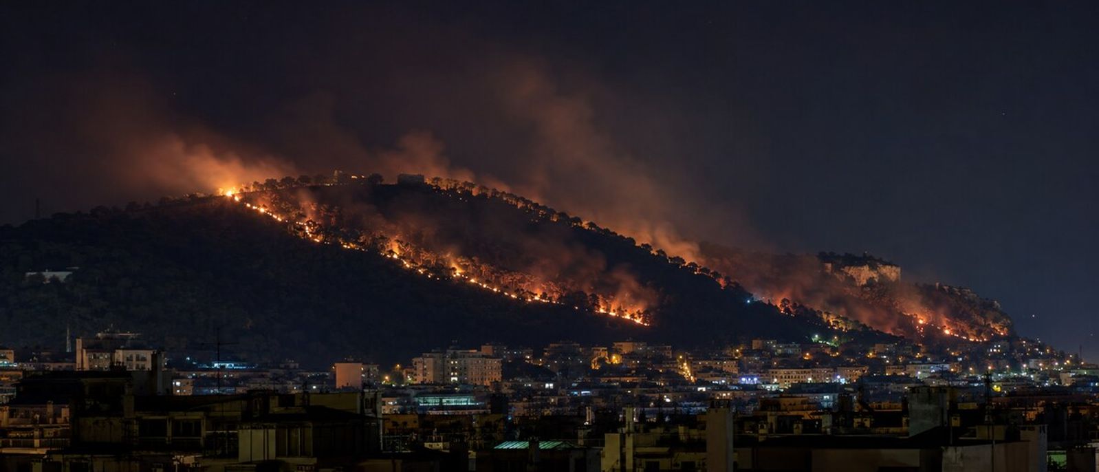 Ligne de feu nocturne progressant sur une colline boisée dominant les quartiers éclairés de Nice