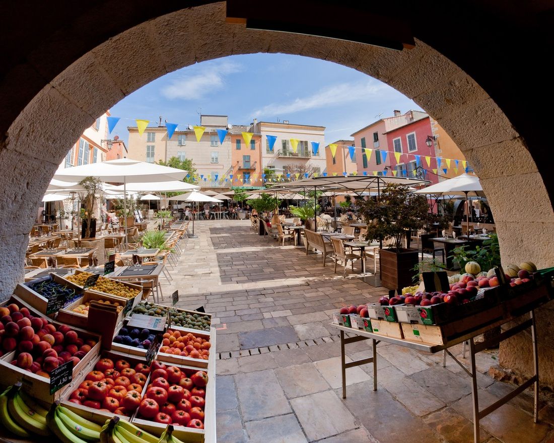 Place des Arcades à Valbonne vue sous une arche, avec façades colorées, terrasses et étals de marché