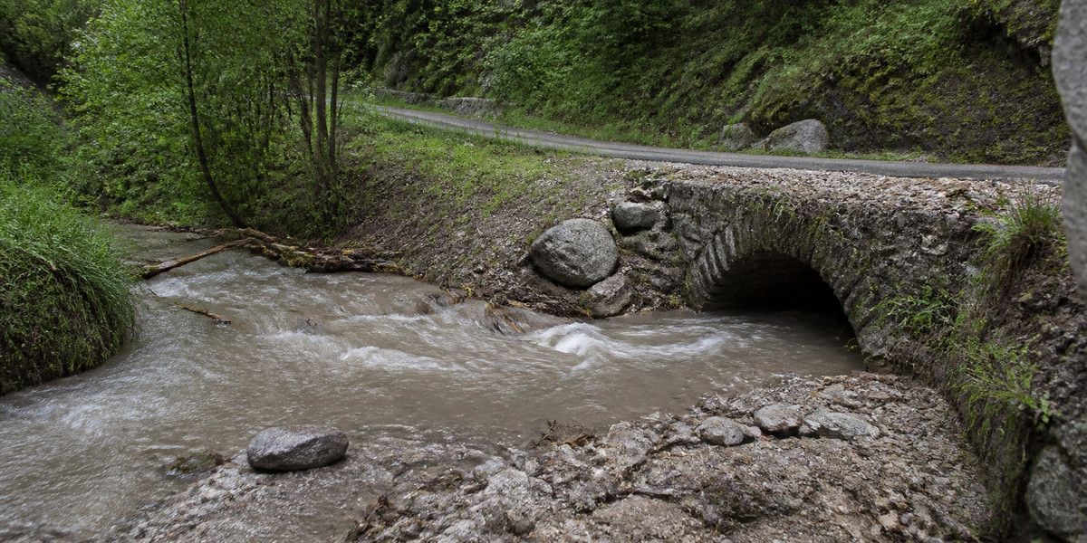 Vallon chargé d’eau boueuse passant sous une petite route de montagne