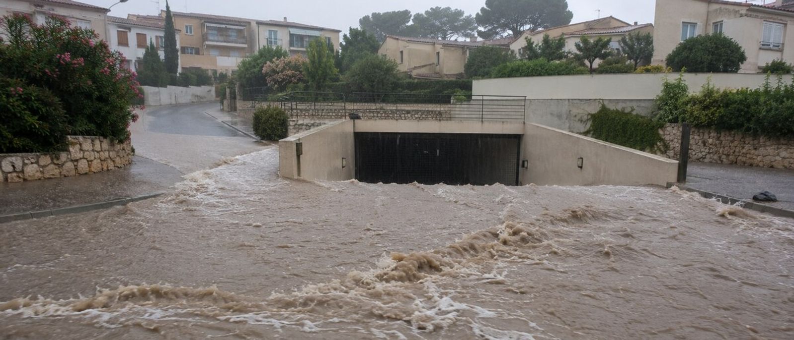 Eaux boueuses ruisselant vers la rampe d’un parking souterrain dans un quartier résidentiel méditerranéen évoquant Antibes