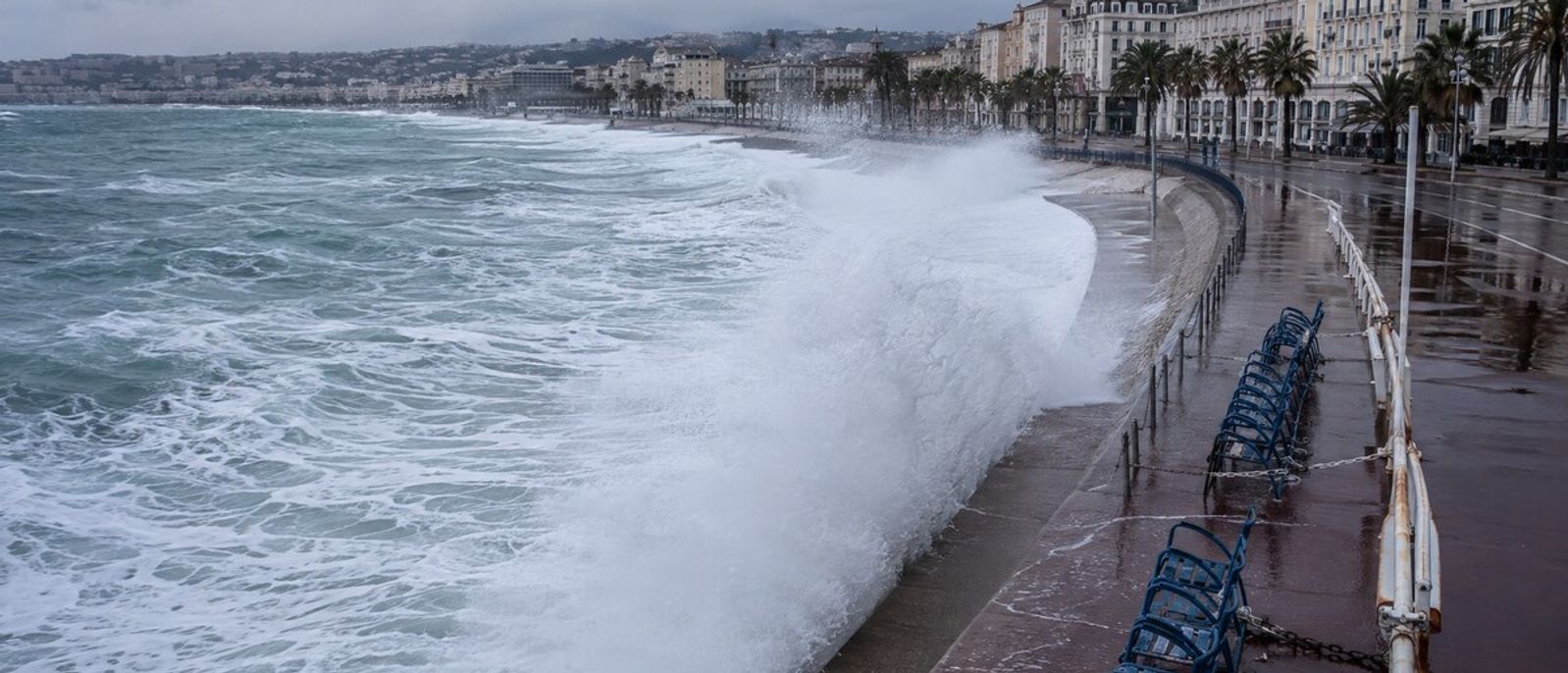 Vague de tempête franchissant le front de mer et projetant des embruns sur les chaises bleues de la Promenade des Anglais