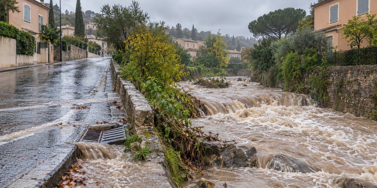 Cours d’eau gonflé longeant une route résidentielle sous une pluie intense, illustration des inondations et du ruissellement