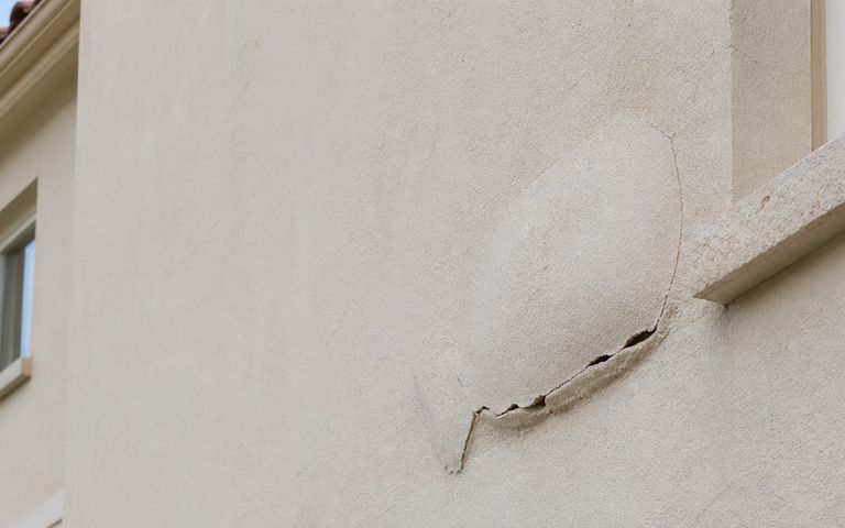 Enduit beige décollé et fissuré sur la façade d’une maison méditerranéenne