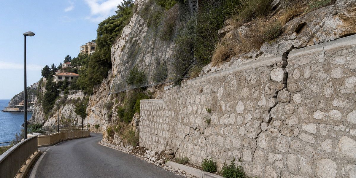 Paroi rocheuse sécurisée et mur de soutènement fissuré sur une route littorale de Roquebrune-Cap-Martin.