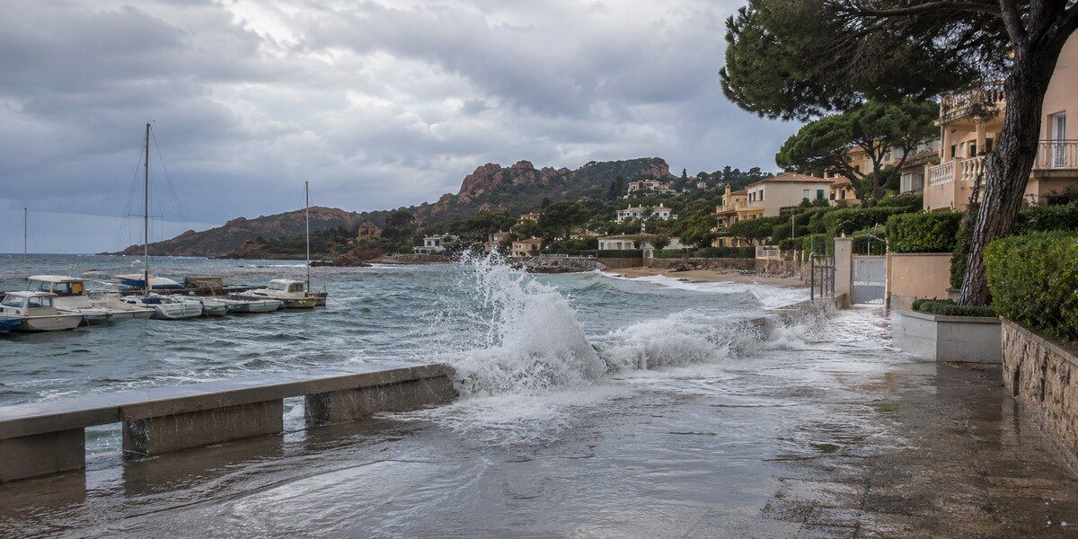 Vagues franchissant un muret côtier et recouvrant une promenade en bord de mer dans un environnement évoquant La Napoule