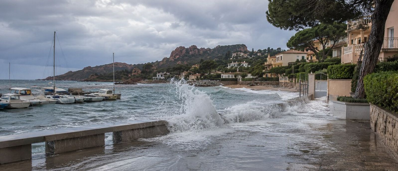 Vagues franchissant un muret côtier et recouvrant une promenade en bord de mer dans un environnement évoquant La Napoule