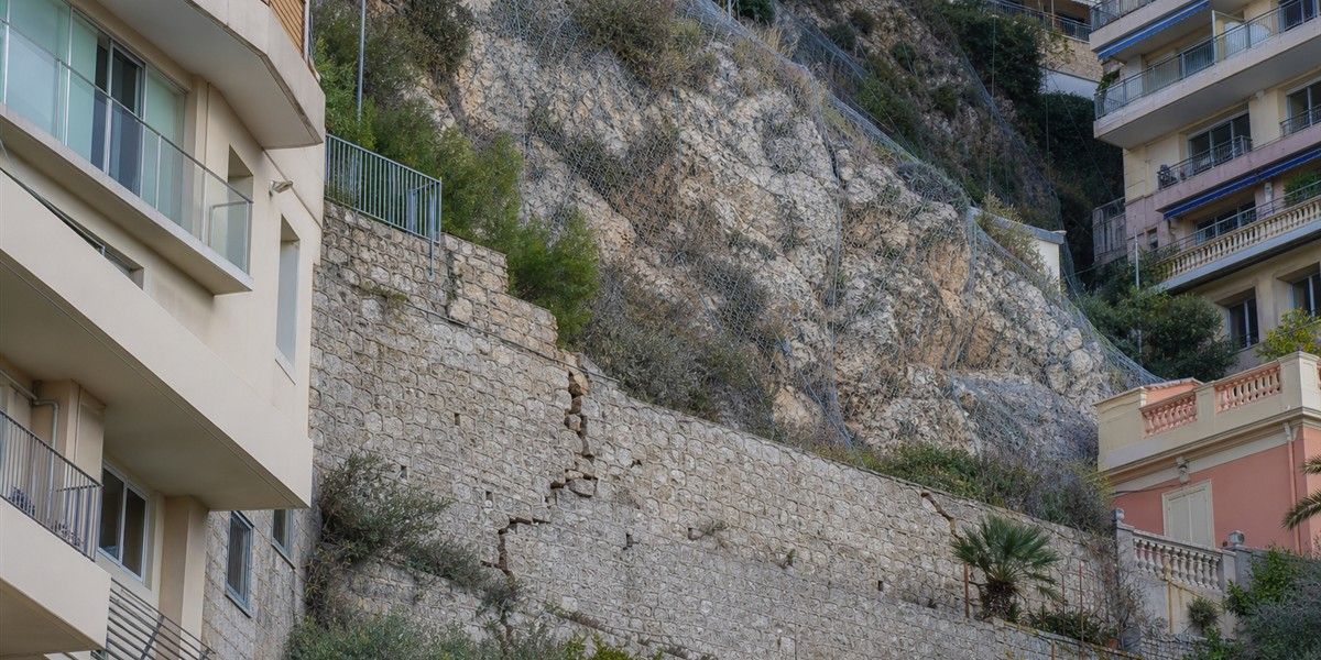 Mur de soutènement fissuré et talus rocheux sécurisé sur un versant urbanisé évoquant Beausoleil
