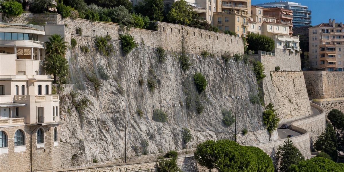 Paroi rocheuse sécurisée et mur de soutènement dominant des immeubles de Monaco, illustrant le risque de chute de blocs