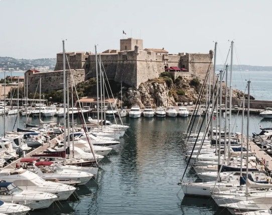 Vue panoramique du Vieil Antibes et de ses remparts dominant la Méditerranée, avec le Port Vauban, les toitures anciennes et le Cap d’Antibes en arrière-plan