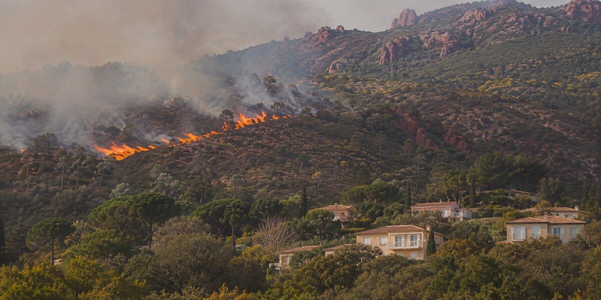 Feu de forêt en journée sur une colline de roches rouges proche de villas et de végétation méditerranéenne évoquant Mandelieu-la-Napoule