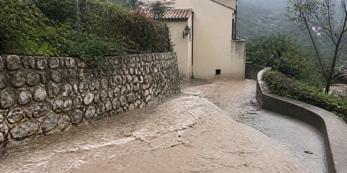 Ruissellement boueux descendant une voie en pente bordée de murs en pierre