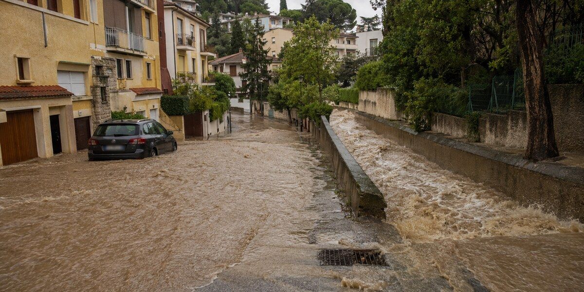 Eaux boueuses envahissant une rue en pente et un vallon urbanisé dans un environnement méditerranéen évoquant Le Cannet