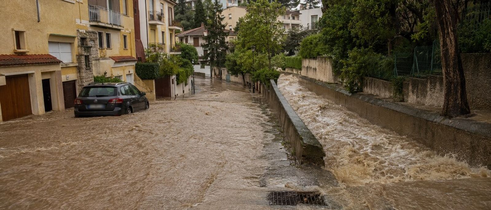 Eaux boueuses envahissant une rue en pente et un vallon urbanisé dans un environnement méditerranéen évoquant Le Cannet