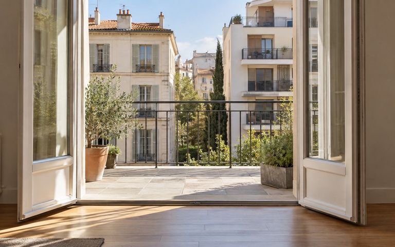 Portes-fenêtres ouvertes sur une terrasse avec vue sur des immeubles résidentiels de styles différents.