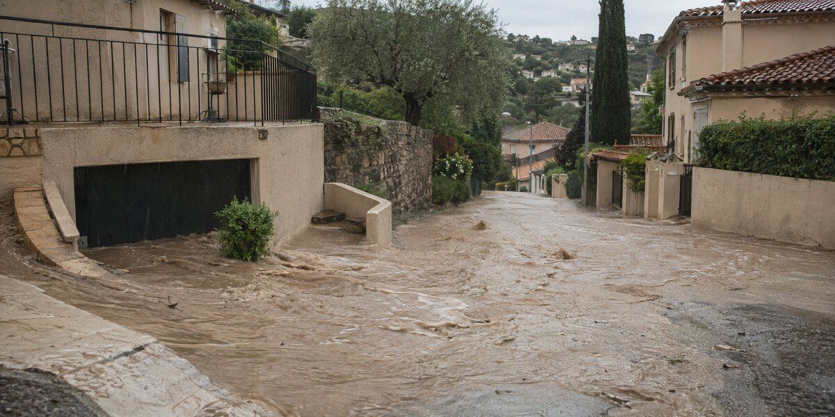 Ruissellement intense et eaux boueuses envahissant une rue en pente dans un environnement résidentiel méditerranéen évoquant Grasse