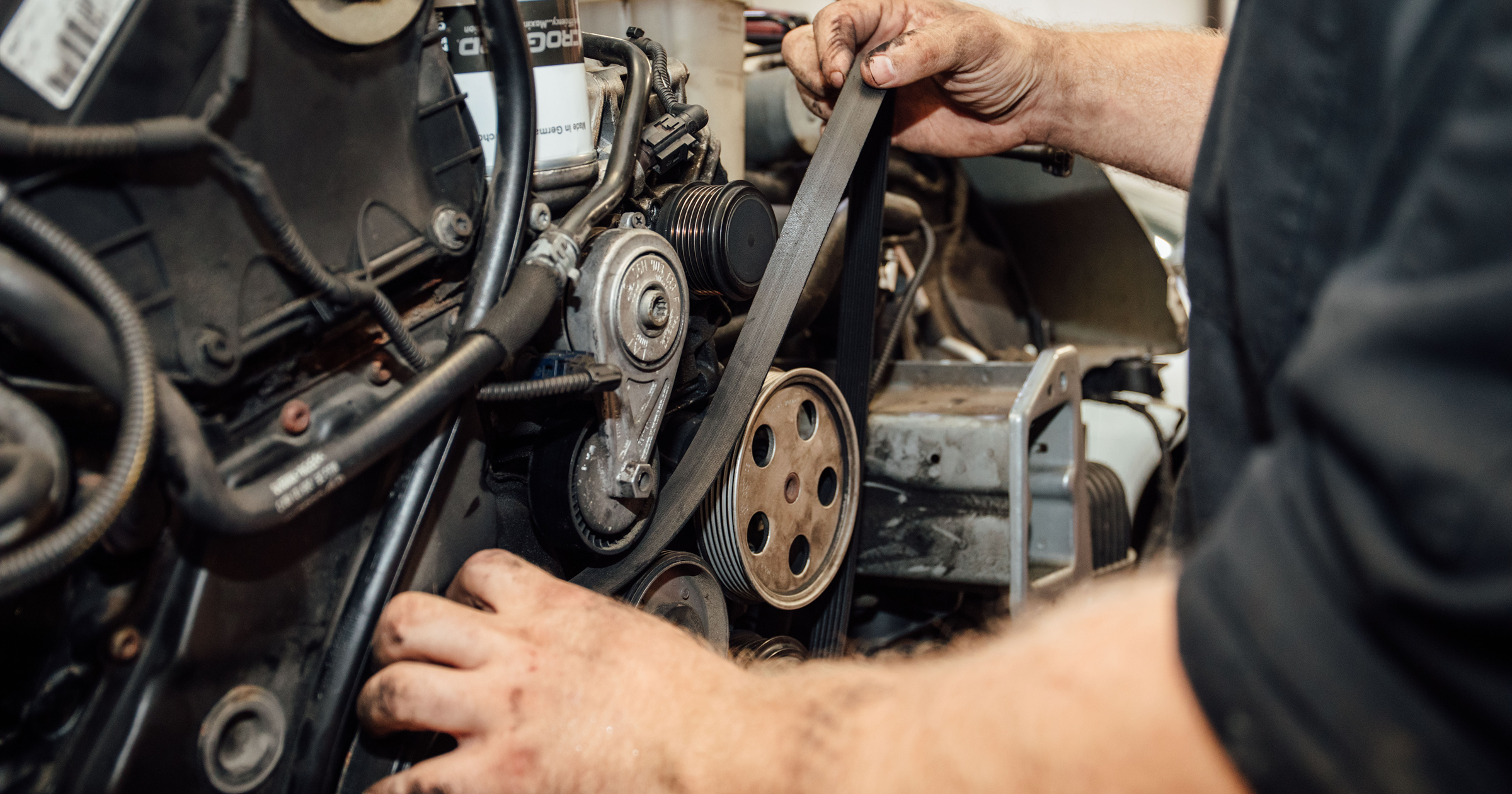 Mechanic installing a serpentine belt on a fleet vehicle engine during maintenance service, inspecting pulleys and components to ensure proper preventive maintenance and uptime.