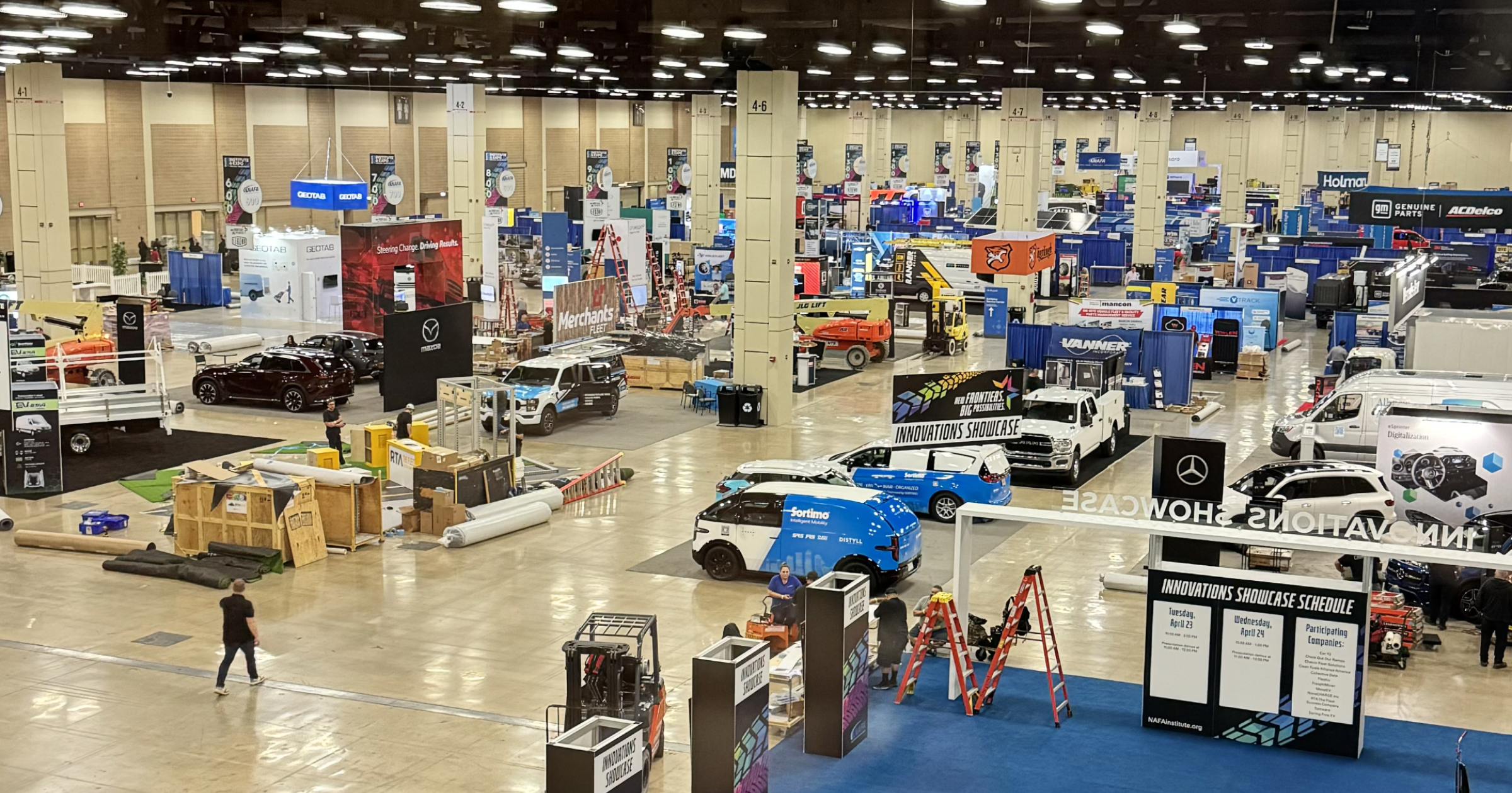 Wide view of a busy expo hall floor at a fleet management trade show, featuring booths, networking spaces, and industry displays.