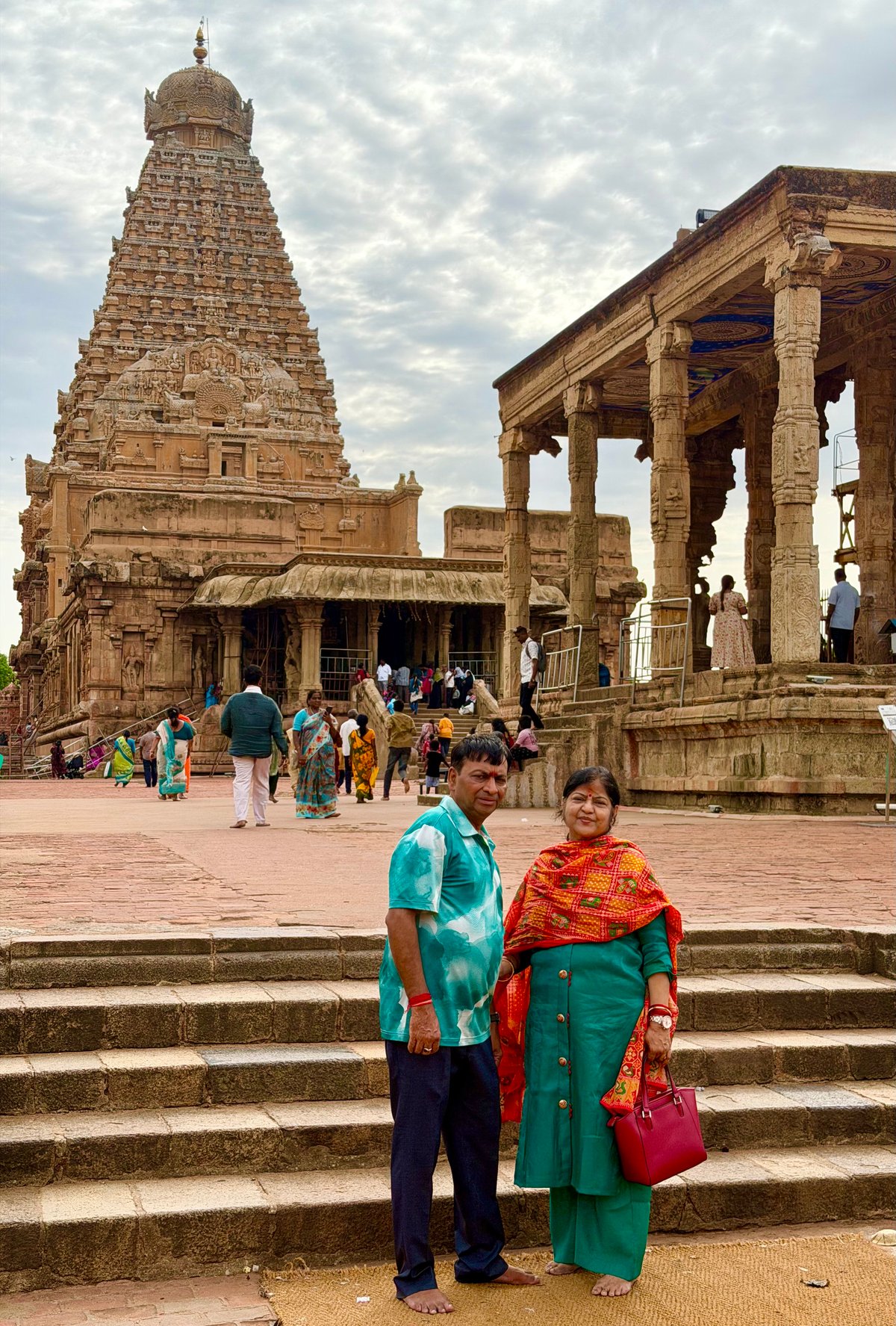 Ma and Papa in the courtyard of Brihadeeswarar — the great vimana rising behind them. A pilgrimage more than a thousand years in the making, finally made.
