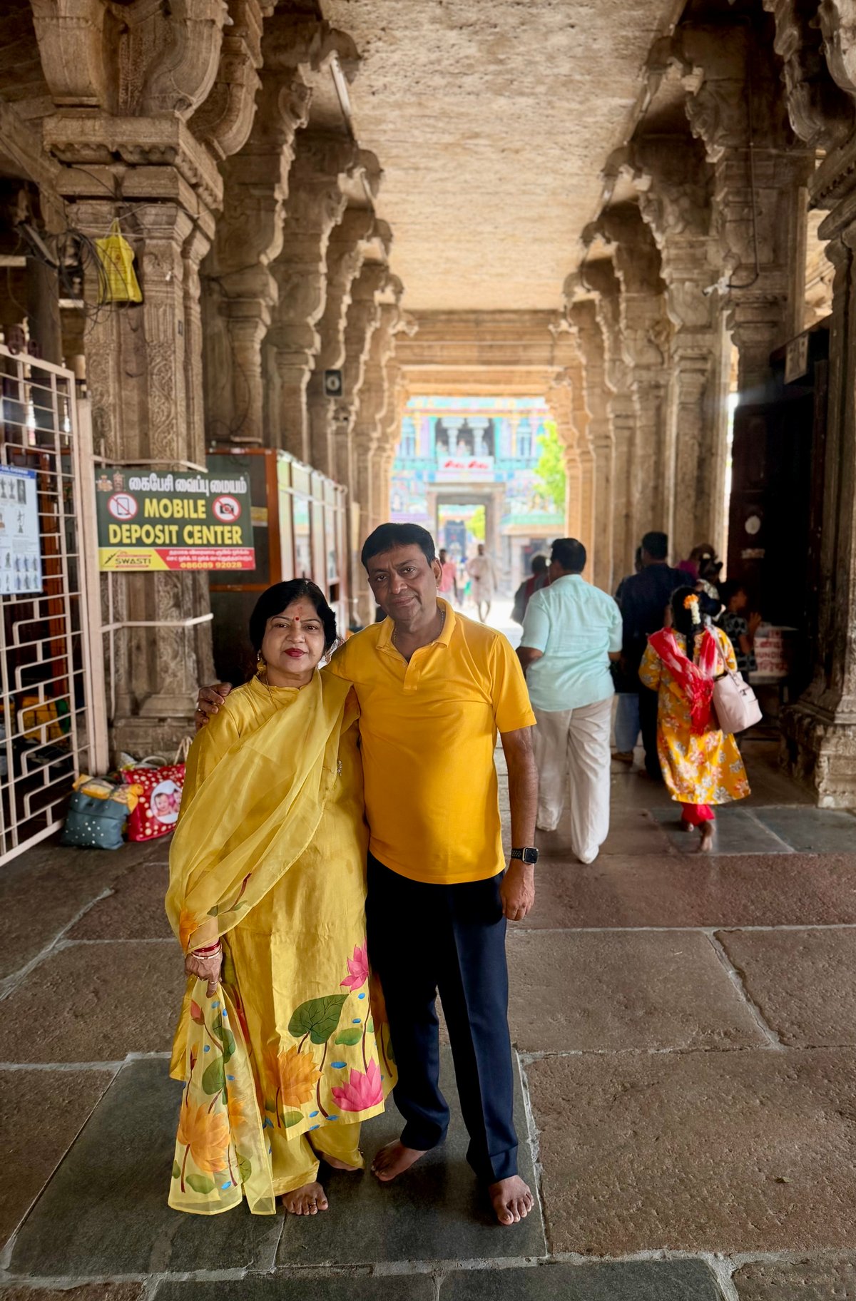 Ma and Papa in the ancient stone corridors of Jambukeswarar Temple — one of the Pancha Bhuta Stalas, dedicated to the water element. The colonnaded mandapam stretches back toward the gopuram, its carved pillars worn smooth by centuries of devotees.