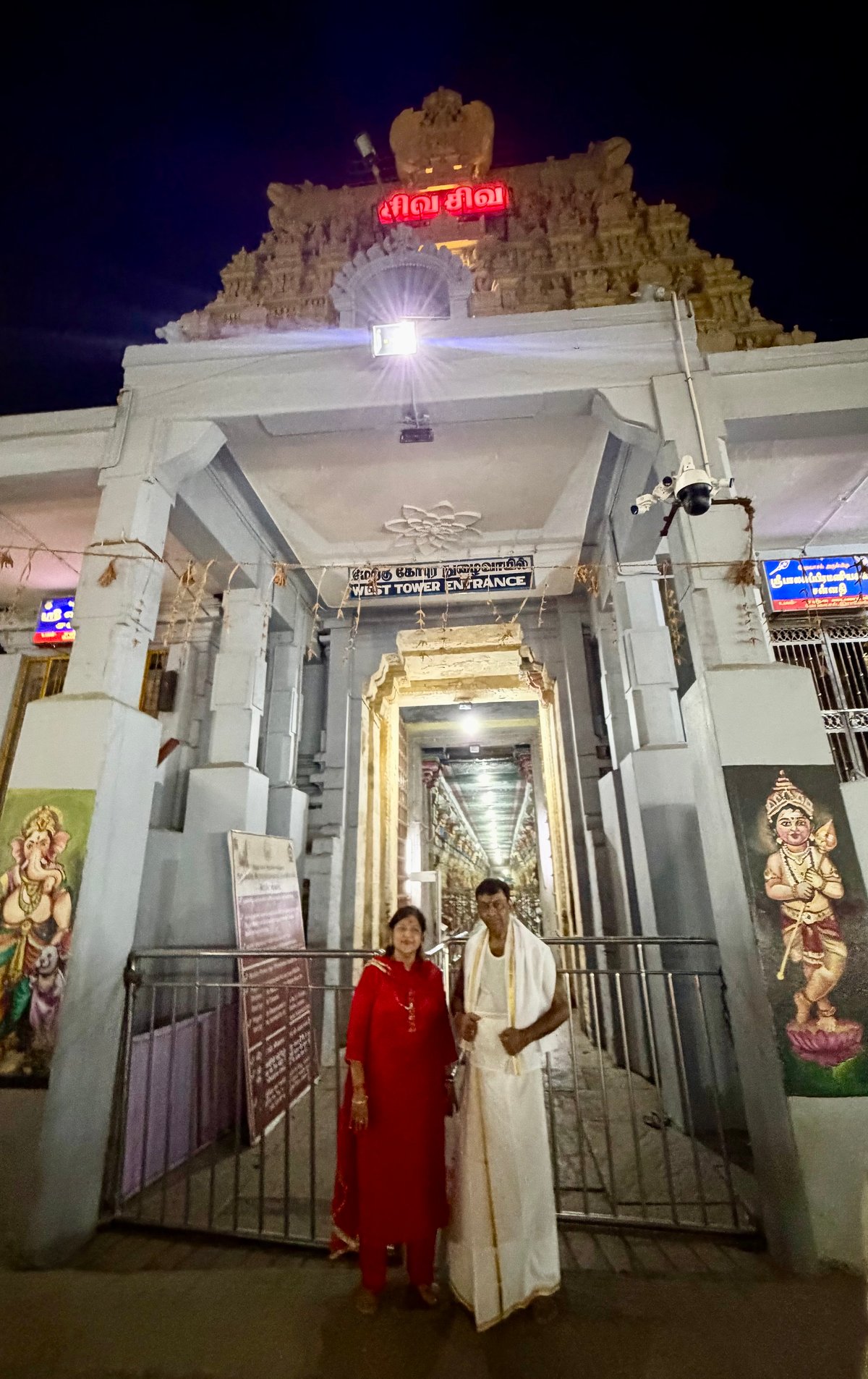 Ma and Papa at the West Tower entrance of Ramanathaswamy Temple, late at night — the long corridor glowing behind them, the day's darshan finally done.