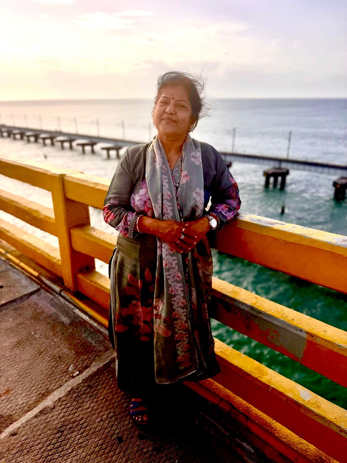 Ma at golden hour on the Pamban Bridge — the sea wind in her hair, the bridge receding into the haze behind her, the sky going soft at the edges. Some moments don't need explaining.