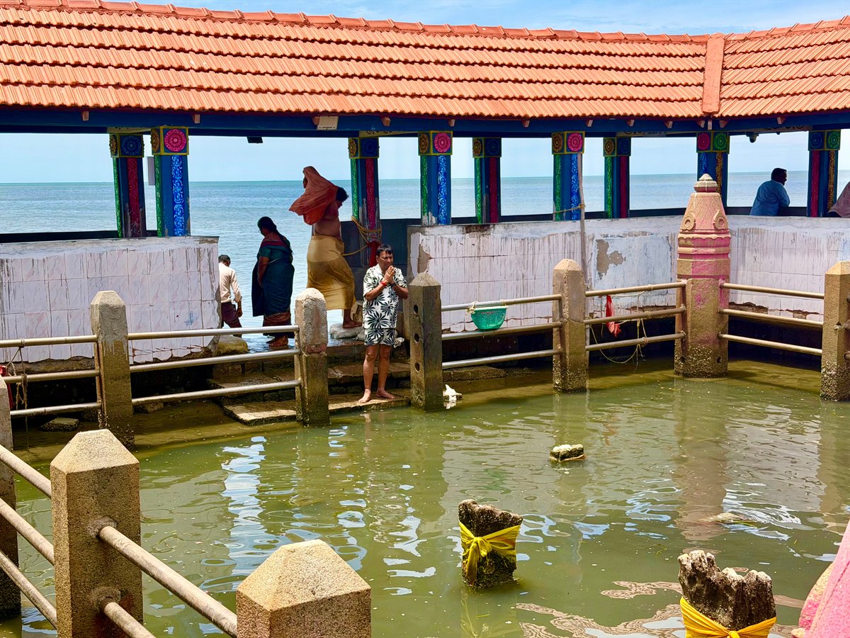 Papa in prayer at the Navagraha kund — hands folded, the sea behind him, the nine submerged planetary stones around him. Quiet and complete.