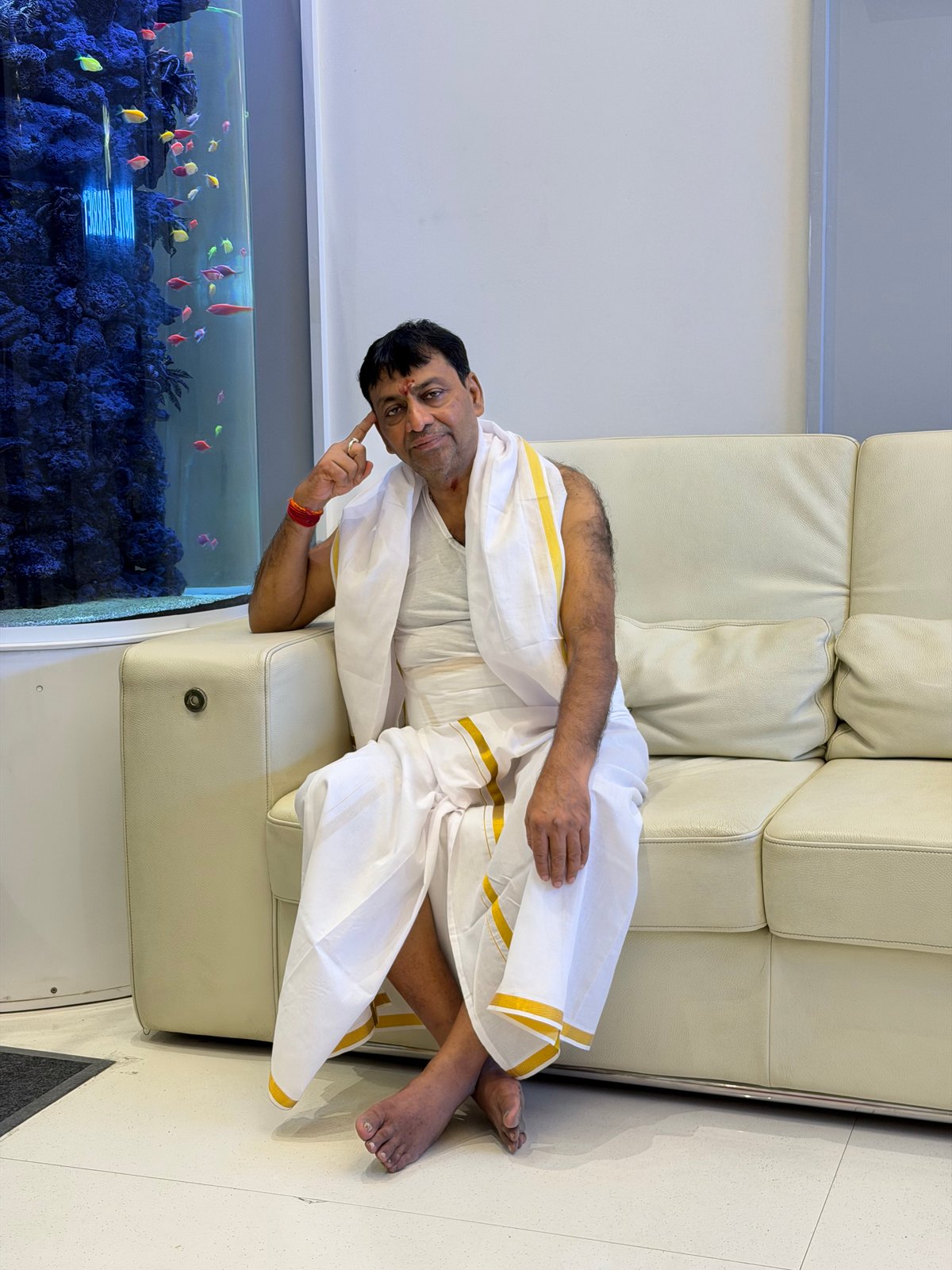 Back at the hotel after the 22 theerthams — still in dhoti, lounging beside the fish tank with the look of someone who has had an unusually complete day. There's a particular kind of peace that comes after a full pilgrimage. This is what it looks like.