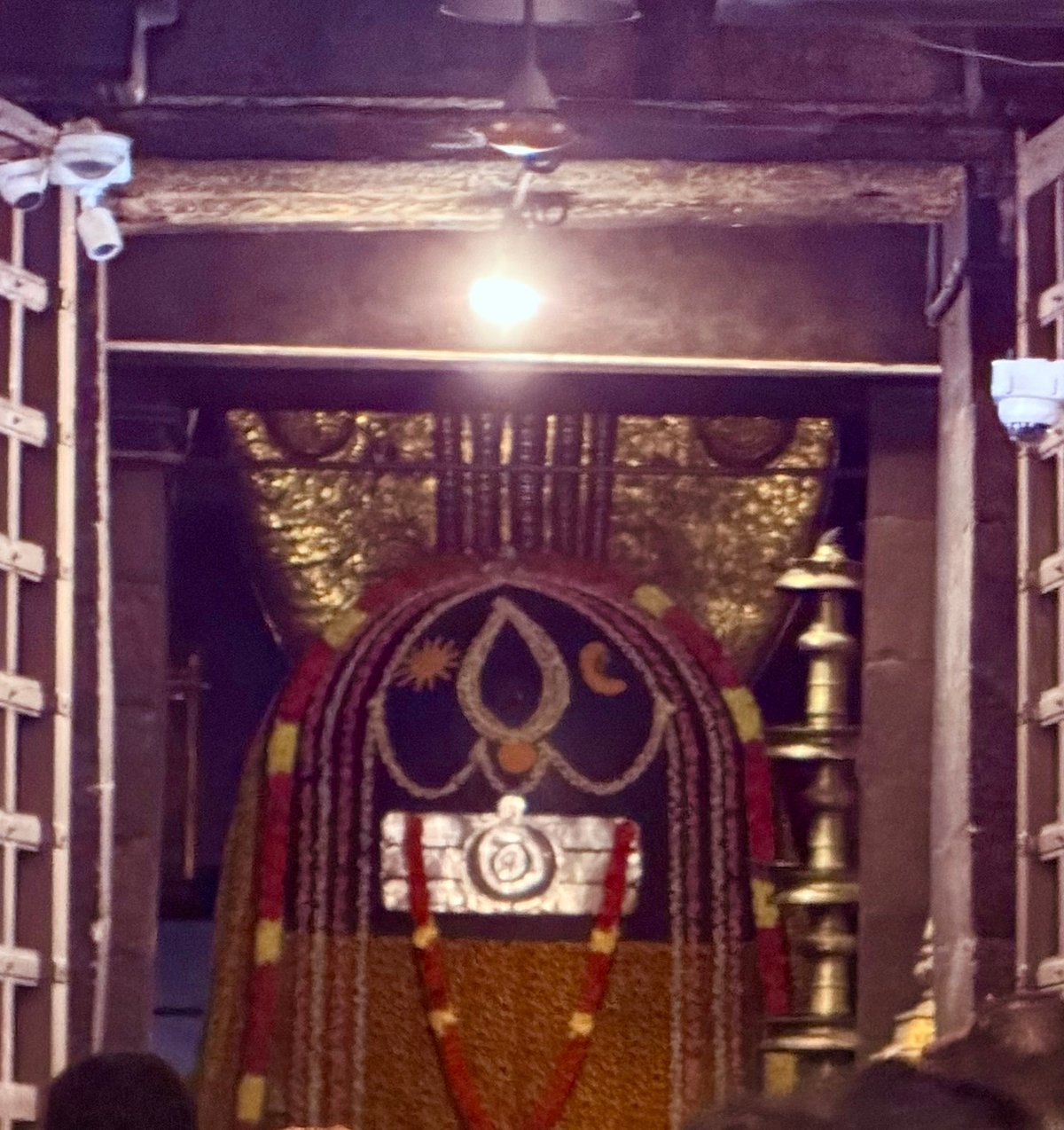 The sanctum of Brihadeeswarar — the deity adorned with silk, marigold, and sacred ash, lit by a single lamp in the dark. The kind of sight that stays with you.
