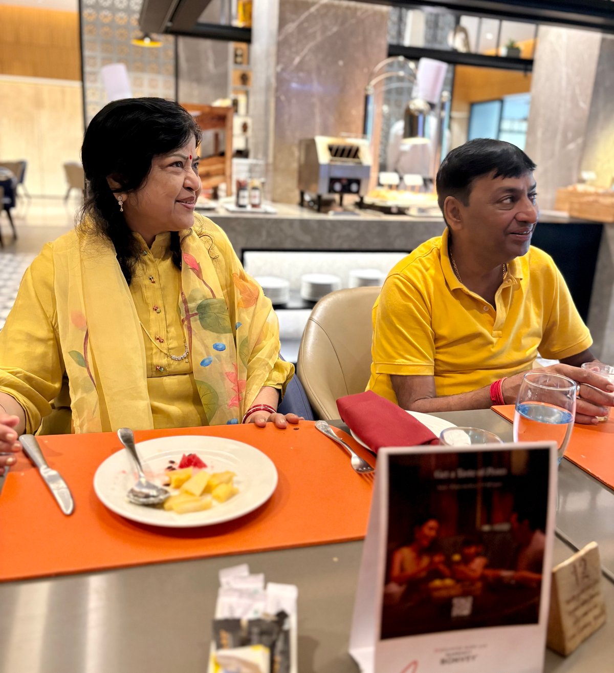 Breakfast at the Courtyard by Marriott, Trichy — Ma and Papa in matching yellow, laughing at something just out of frame. The calm after days of temples and travel.