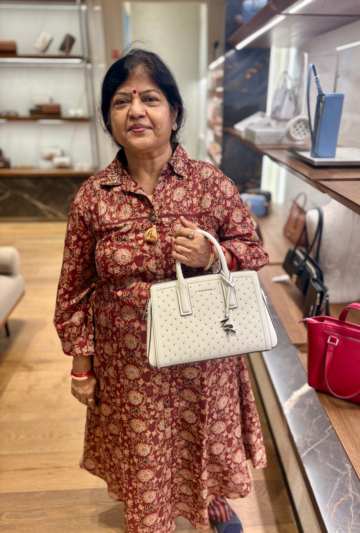 Ma trying out a Michael Kors bag at the airport shops — a little retail pause on the journey.