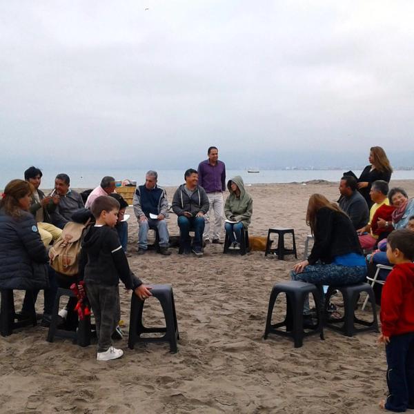 Personas reunidas en círculo sobre la arena de la playa en una reunión de oración en Coquimbo