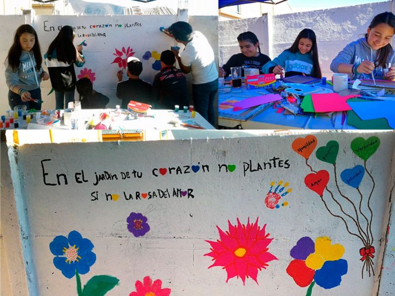 Prejóvenes pintan un mural con flores y la frase «En el jardín de tu corazón no plantes sino la rosa del amor»