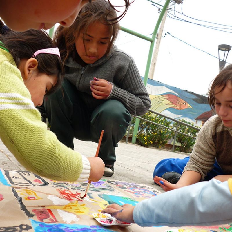 Niñas y niños pintan juntos un gran dibujo sobre el suelo durante una actividad artística