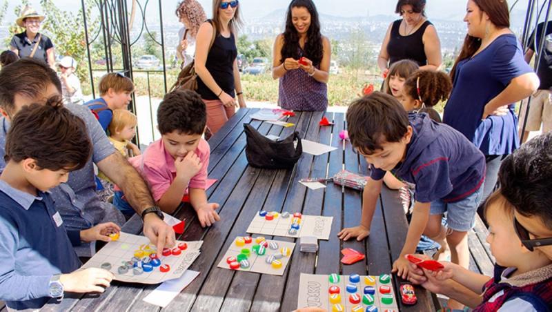 Niñas y niños juegan y aprenden en torno a una mesa durante una clase de niños, con la ciudad de fondo