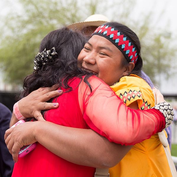 Dos mujeres se abrazan con alegría, una con vestimenta tradicional mapuche