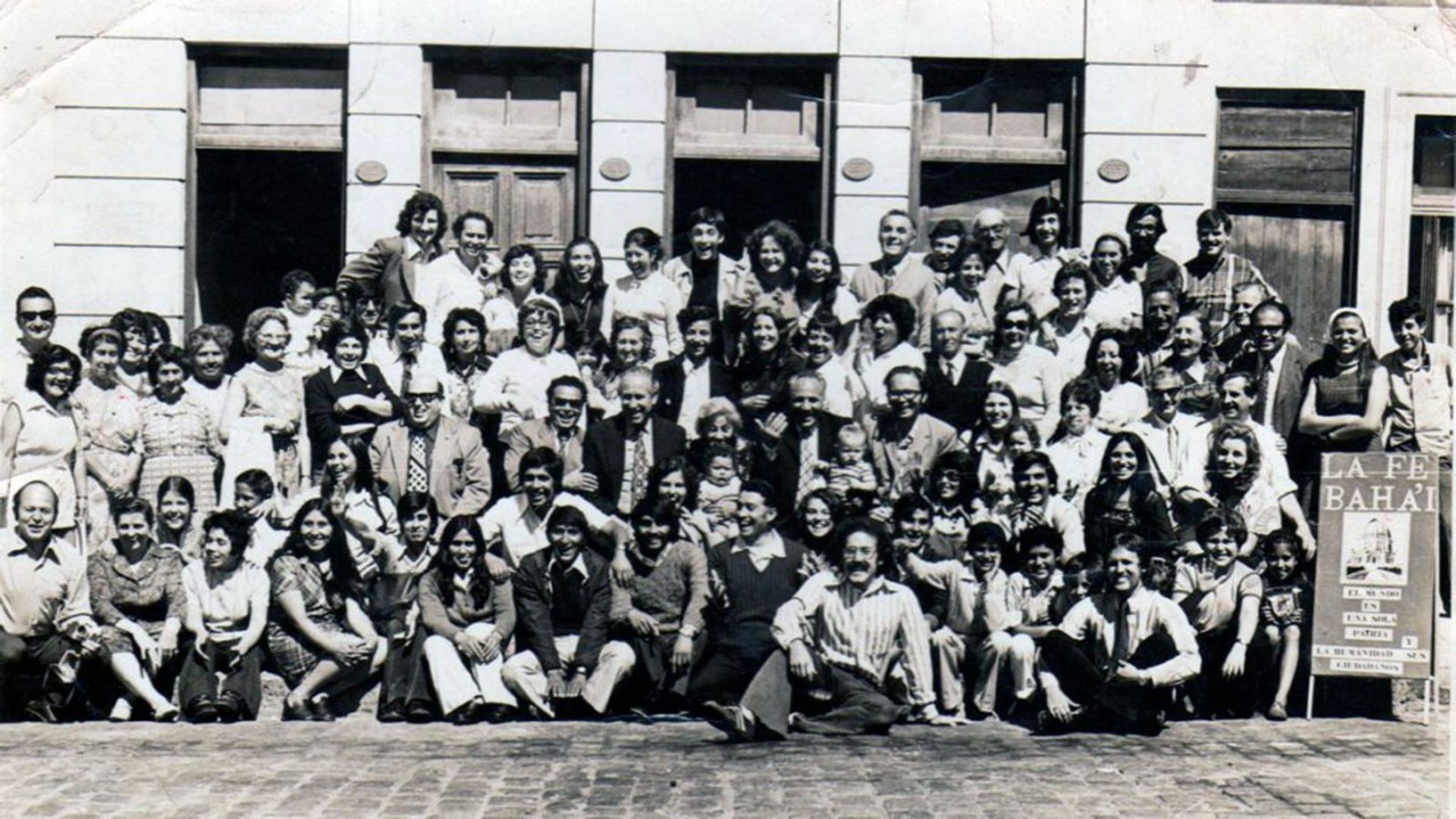 Encuentro histórico de la comunidad bahá’í de Chile en los años setenta, frente al cartel «La Fe Bahá’í»