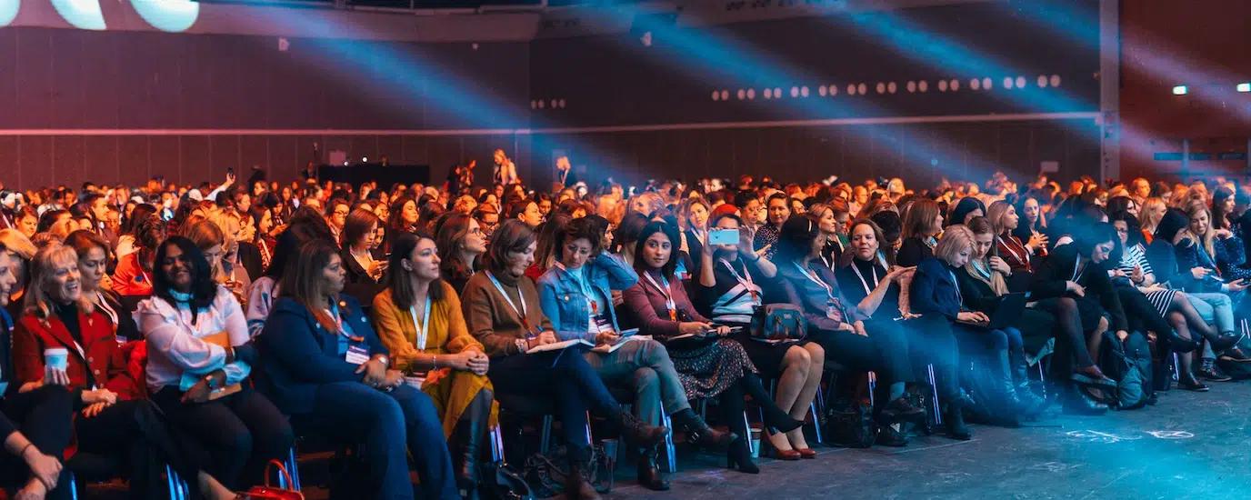 Vibrant image of a diverse audience seated in a large auditorium, highlighted by dynamic stage lighting
