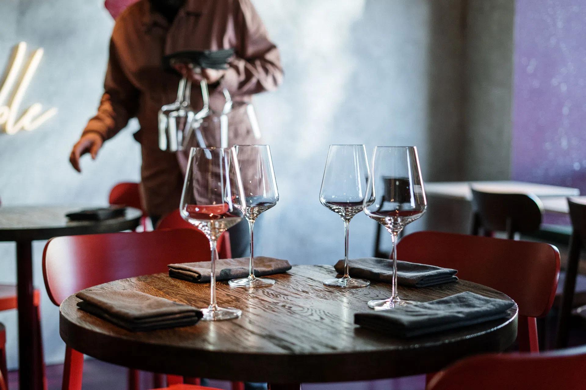 Interior view of a café with neatly arranged tables, wine glasses, and a waiter in the background
