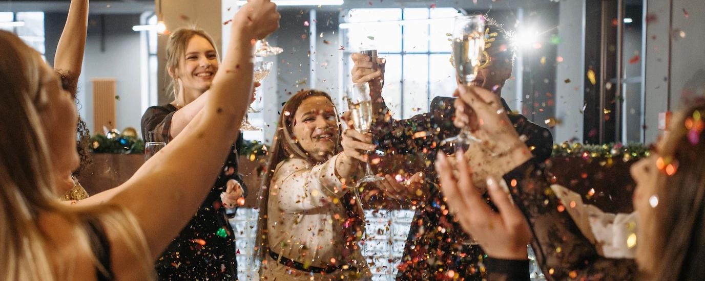 A diverse group of coworker celebrating in the office with champagne and confetti.