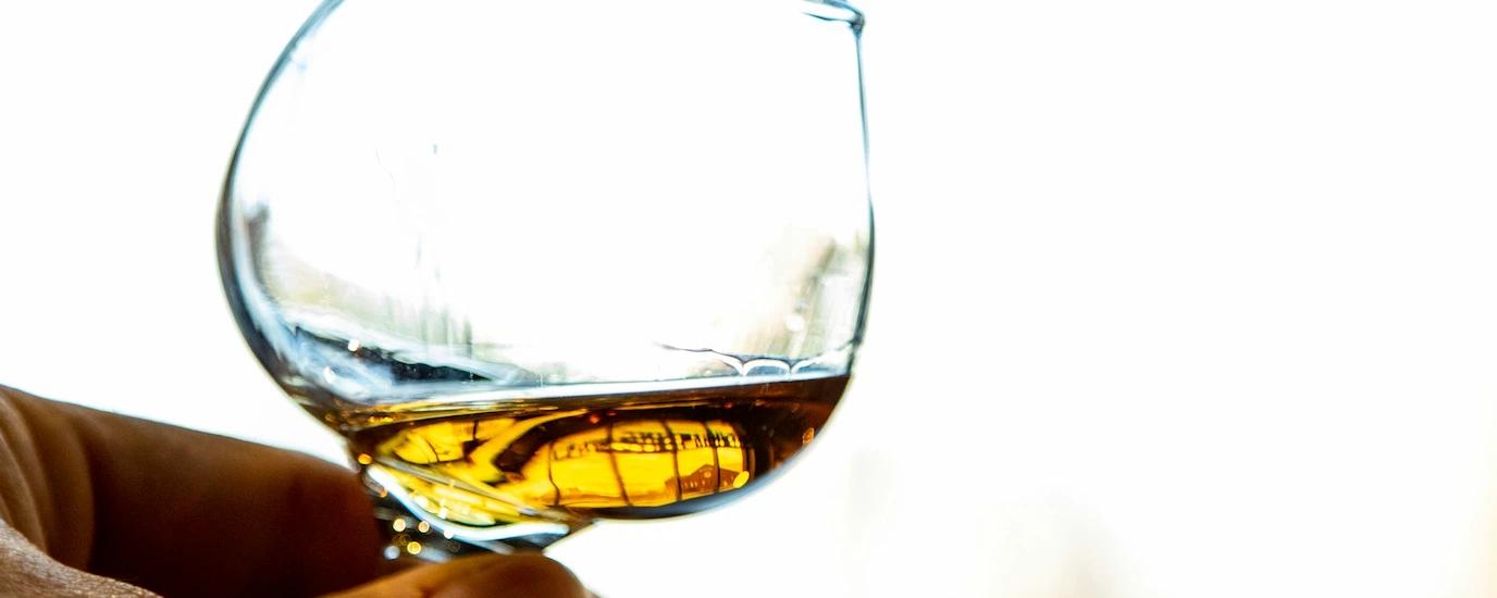 A hand holding a whiskey snifter glass by the stem