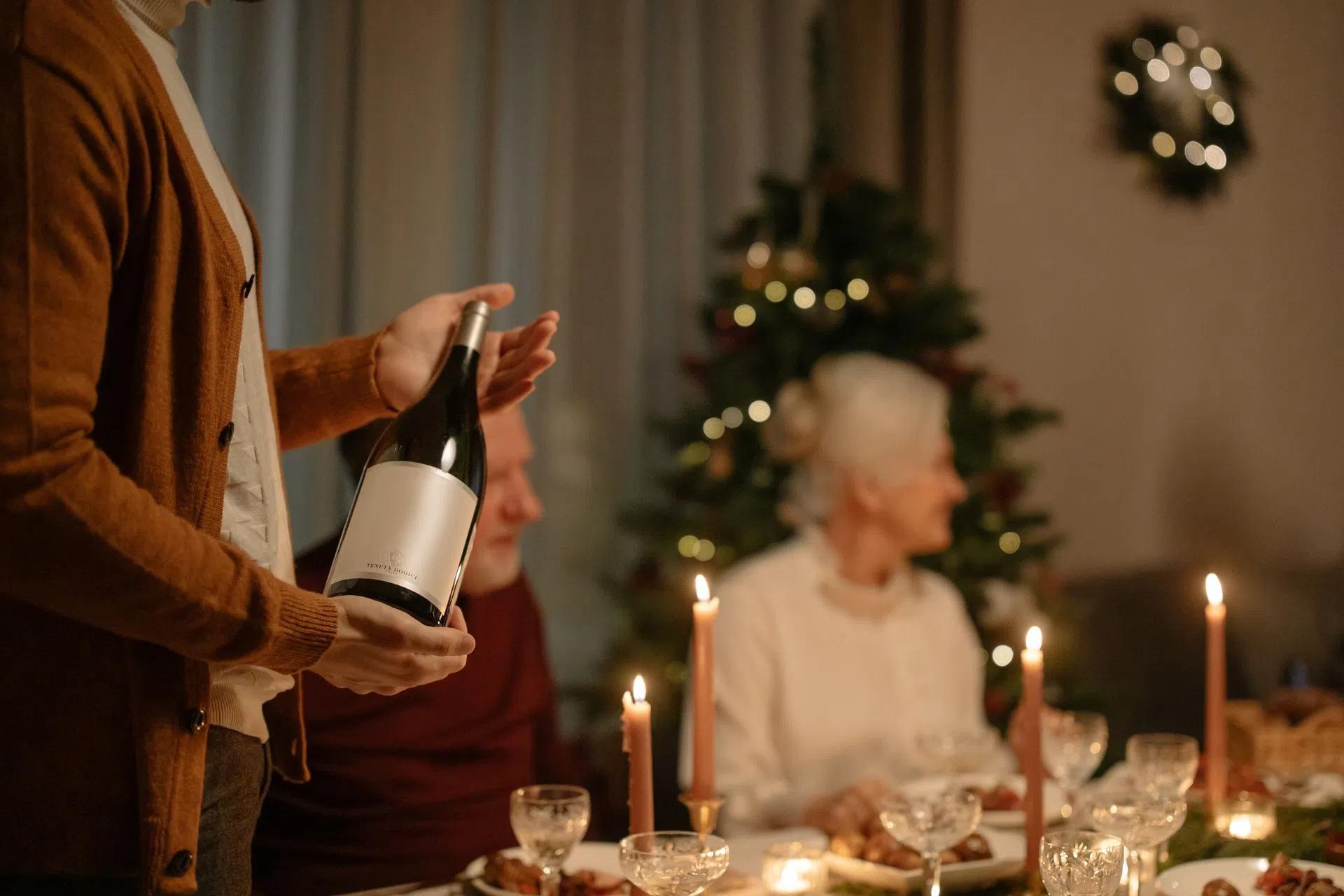 A person holding a wine glass during a cozy family gathering around a dinner table during the Christmas season