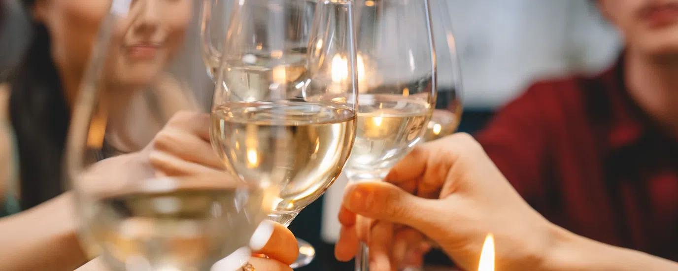 Group of friends toasting with white wine glasses indoor, creating a warm and festive atmosphere