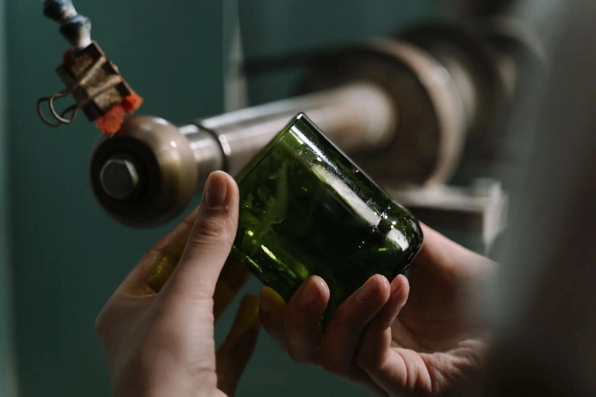 Hands crafting a glass bottle with precision on a cutting machine in a workshop