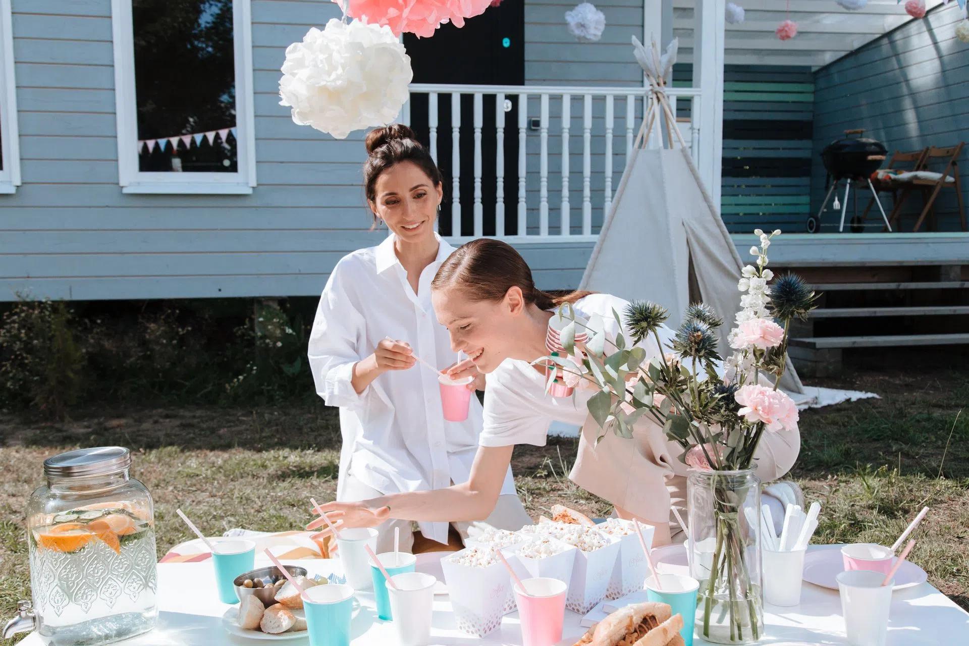 Two women enjoying a backyard party with food and floral decorations on a sunny day.