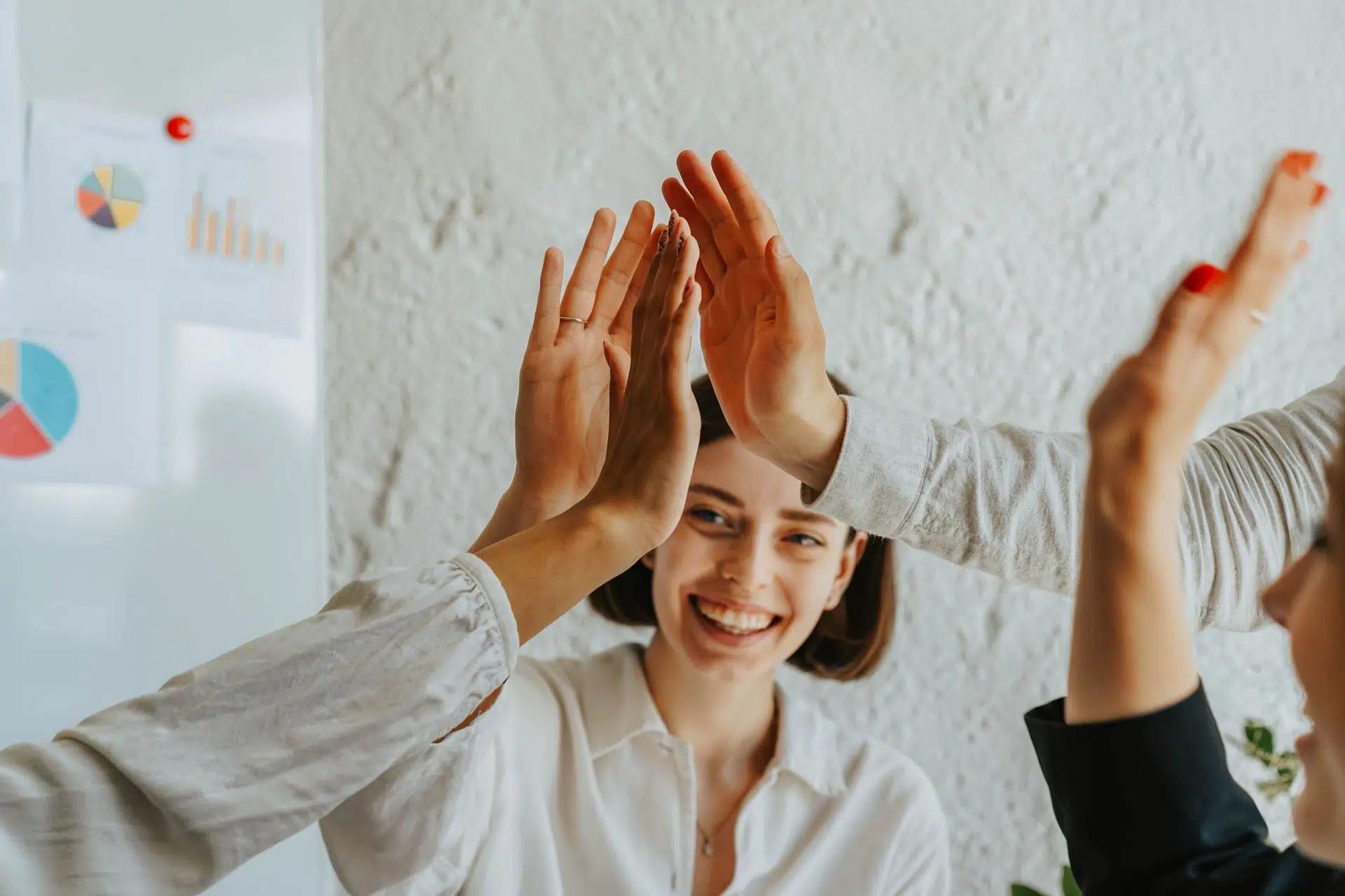 Group of smiling adults engaging in a teamwork high five celebration in an office setting