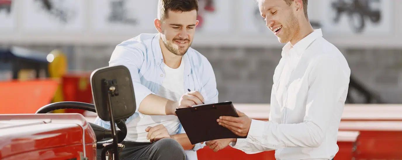 Two men discussing tractor purchase, collaborating outdoors with clipboard