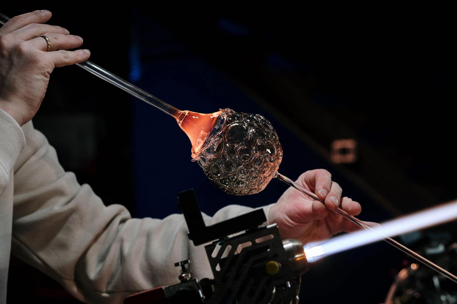 Close-up of a craftsman skillfully working with glass and flame in a dimly lit studio