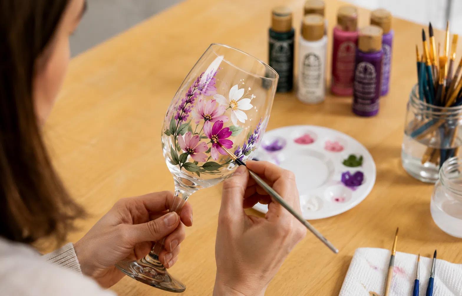 A woman painting a floral design on a wine glass
