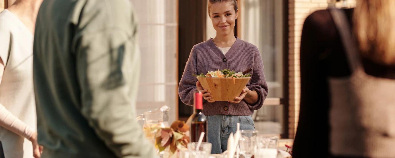 A woman smiling while holding a bowl of salad during an outdoor gathering with friends