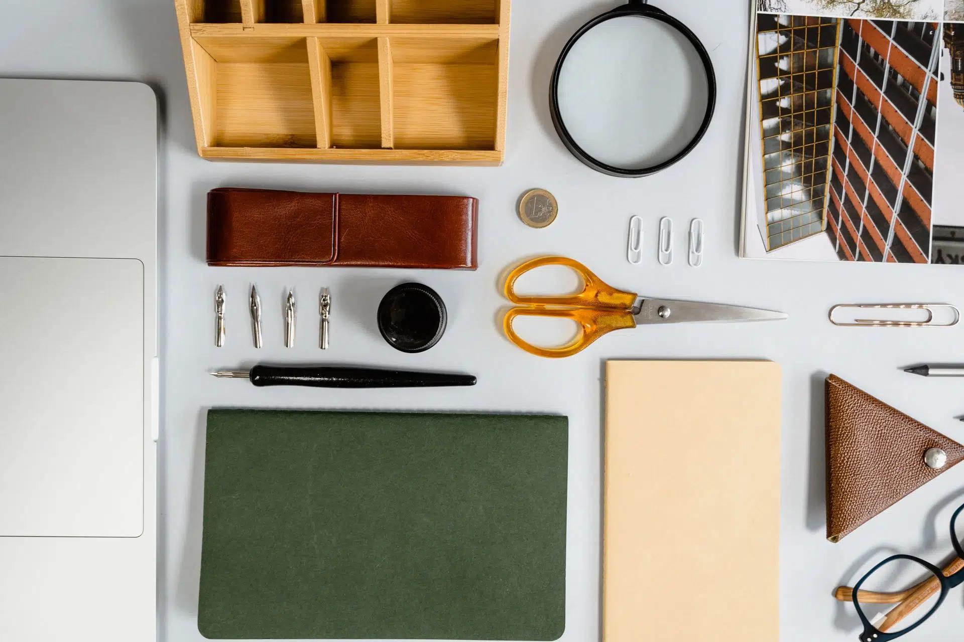 Flat lay of neatly arranged office supplies on a white desk, including scissors, notebook, and laptop